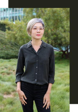 Eileen Chao, MA, intimacy coach and surrogate partner in San Francisco, standing outdoors with soft green foliage behind her