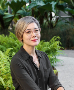 Eileen Chao, sex and relationship coach serving San Francisco, Marin, the East Bay, and the Peninsula. She's sitting with green ferns behind her.
